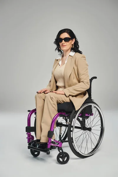 Mujer guapa con discapacidad de movilidad en silla de ruedas sentada en silla de ruedas con gafas de sol - foto de stock