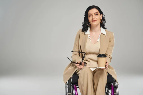 Attraente donna disabile in abito pastello con occhiali da sole e caffè e guardando la fotocamera — Foto stock