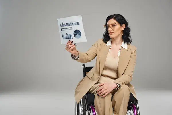 Chère belle femme avec un handicap de mobilité dans les lunettes regardant des graphiques en fauteuil roulant — Photo de stock