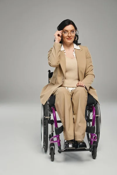 Attraente bruna donna disabile in elegante vestito in sedia a rotelle con occhiali guardando la fotocamera — Foto stock
