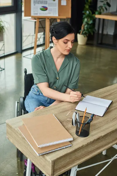 Gut aussehende Geschäftsfrau mit Behinderung sitzt im Rollstuhl und schaut in ihr Notizbuch — Stockfoto