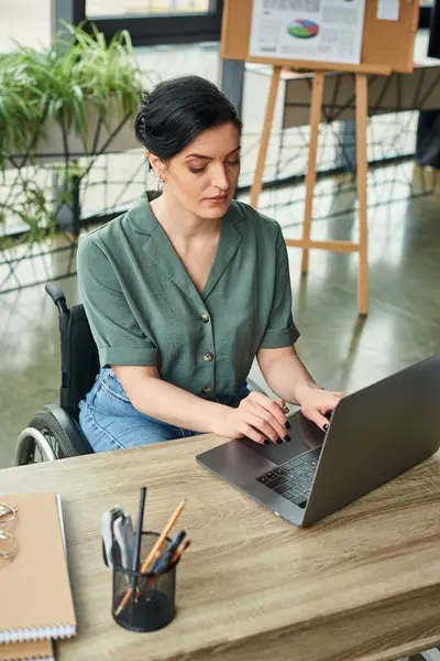 Mulher de negócios de boa aparência em traje casual em cadeira de rodas trabalhando em seu laptop enquanto no escritório — Fotografia de Stock