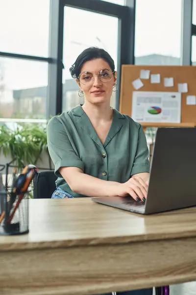 Mulher deficiente atraente em roupas casuais com óculos trabalhando no laptop enquanto no escritório — Fotografia de Stock