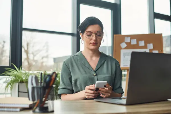 Disabled beautiful businesswoman with glasses in casual attire looking at her phone while in office — Stock Photo