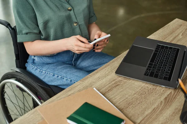 Cropped view of disabled woman in casual attire sitting in wheelchair and working on her laptop — Stock Photo