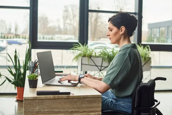 Confident hard working businesswoman in casual attire in wheelchair working on laptop in office — Stock Photo