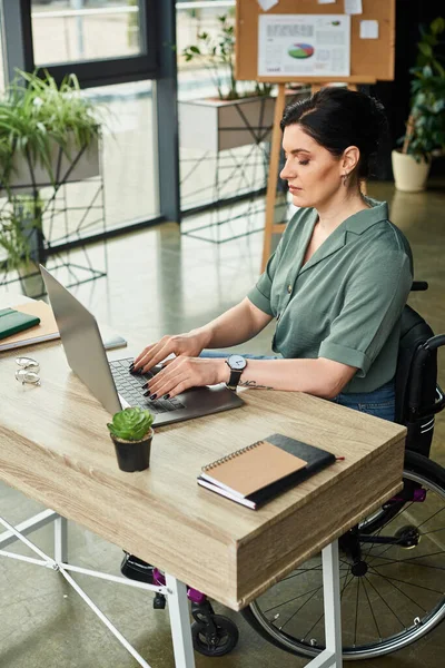 Mulher de negócios atraente com deficiência em cadeira de rodas trabalhando duro em seu laptop no escritório — Fotografia de Stock