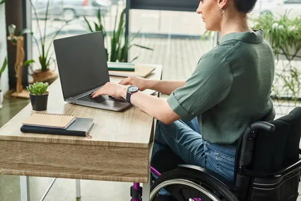 Attractive disabled businesswoman in casual attire in wheelchair sitting at laptop working in office — Stock Photo