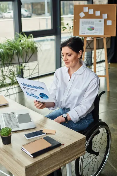 Allegra donna disabile in abbigliamento casual con i capelli scuri guardando la grafica mentre nel suo ufficio — Foto stock