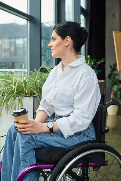 Bella donna d'affari allegra in abbigliamento casual in sedia a rotelle in possesso di caffè mentre in ufficio — Foto stock