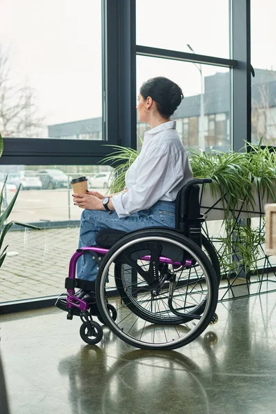 Attrayant dédié femme handicapée en tenue décontractée en fauteuil roulant tenant café tandis que dans le bureau — Photo de stock