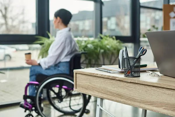 Fokus auf Tisch mit Schreibwaren mit verschwommener behinderter Frau im Rollstuhl auf Hintergrund im Büro — Stockfoto