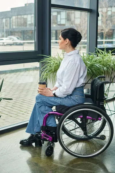 Симпатичная деловая женщина-инвалид в модном наряде в инвалидном кресле держит кофе и смотрит в сторону — стоковое фото