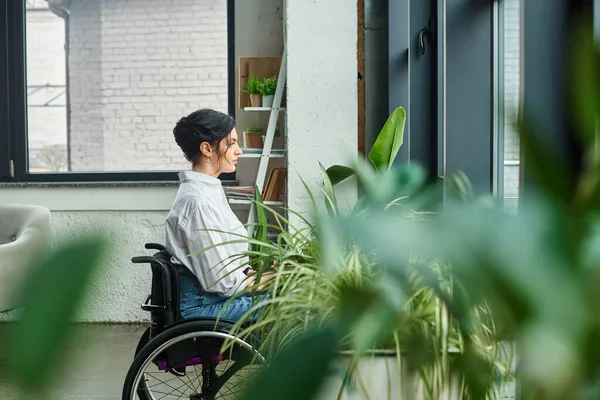 Красивая деловая женщина-инвалид в стильной одежде в инвалидном кресле смотрит вдаль, находясь в офисе — стоковое фото