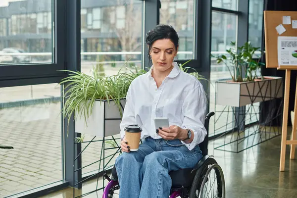 Atractiva morena mujer discapacitada en elegante atuendo en silla de ruedas sosteniendo café y teléfono inteligente - foto de stock