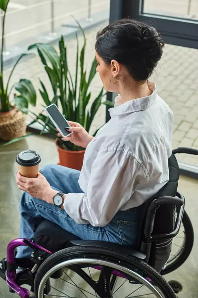 Attrayant dédié femme avec handicap en fauteuil roulant dans une tenue élégante tenant café et téléphone — Photo de stock