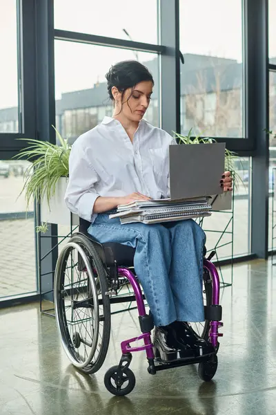 Trabajadora atractiva empresaria con discapacidad de movilidad en silla de ruedas mirando el portátil - foto de stock