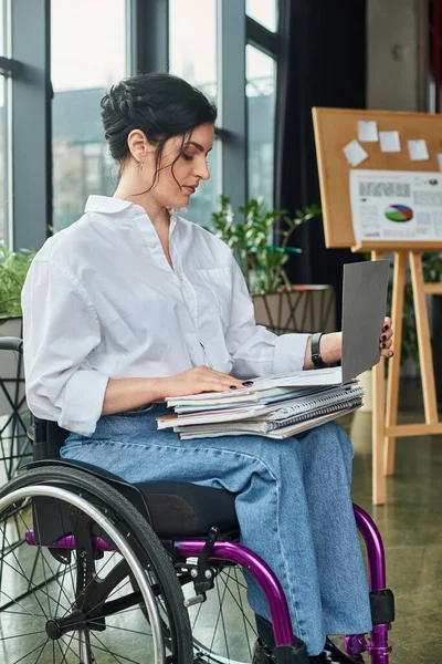 Atraente trabalhador duro empresária deficiente em cadeira de rodas trabalhando em seu laptop com papelada — Fotografia de Stock