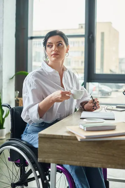 Bella donna dedicata con disabilità in sedia a rotelle bere caffè mentre nel suo ufficio — Foto stock