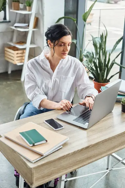 Attractive brunette businesswoman with disability in wheelchair working on her laptop in office — Stock Photo