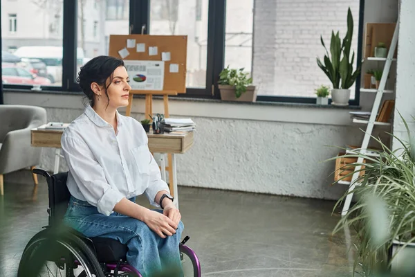Atractiva mujer de negocios con discapacidad de movilidad en atuendo casual en silla de ruedas mirando hacia otro lado - foto de stock