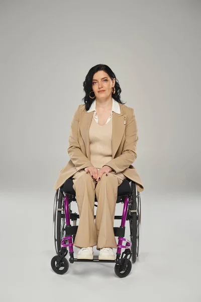 Good looking disabled woman in elegant pastel suit in wheelchair looking straight at camera — Stock Photo