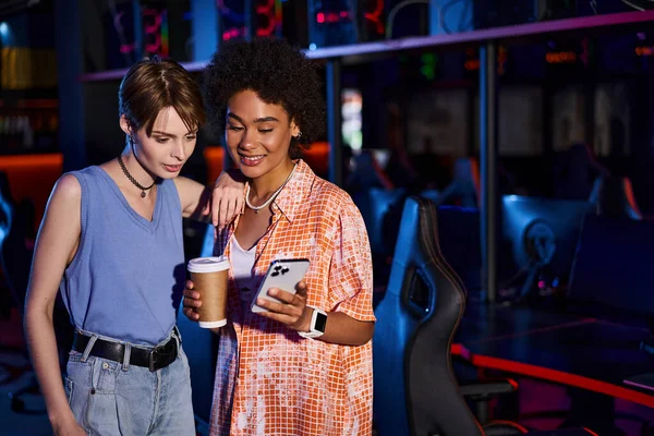 Interracial happy women while browsing phone, their smiling faces illuminated by vibrant light — Stock Photo