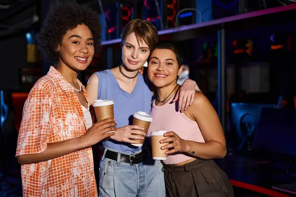 Un grupo de mujeres interracial felices disfrutando de una salida nocturna, con sonrisas cálidas y tazas de café en las manos - foto de stock