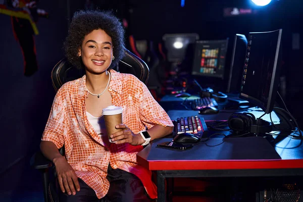 A stylish black woman with a coffee in hand, takes a moment to unwind at her desk with computer — Stock Photo