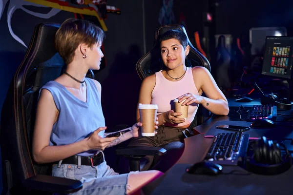 Femme élégante tenant tasse de café et regardant son amie, monde du jeu et cybersport — Photo de stock