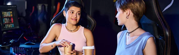Mujer elegante sosteniendo la taza de café y mirando a su amiga, mundo del juego y banner ciberdeporte - foto de stock