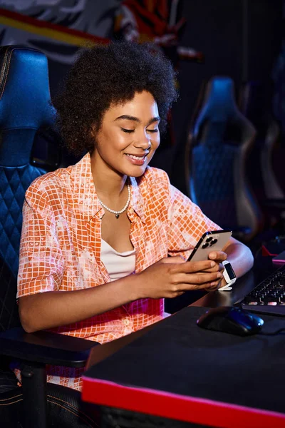 Mujer enfocada se sienta en su computadora, su rostro iluminado por la pantalla azul del teléfono inteligente - foto de stock