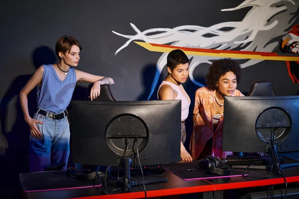 Team of young gamers at a cybersport event, interracial women looking at computer while playing game — Stock Photo