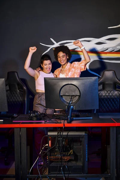 Due donne interrazziali e gioiose che celebrano la vittoria dopo aver vinto nella sala giochi, cybersport — Foto stock