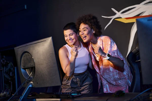 Two interracial and happy women celebrating victory after winning in gaming room, cybersport — Stock Photo