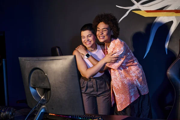 Interracial and happy friends hugging and celebrating victory in gaming room, cybersport game — Stock Photo