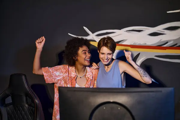 Multicultural happy female friends looking at computer monitor and celebrating victory, cybersport — Stock Photo
