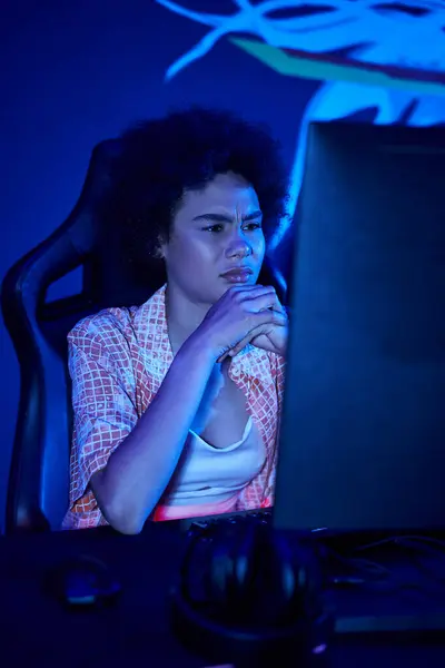 Зосереджена афроамериканська жінка інтенсивно грає у синьо-світлій кімнаті, концепція кіберспорту — стокове фото