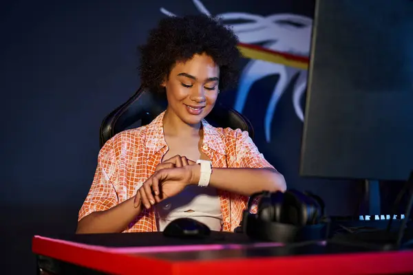 Femme afro-américaine souriante vérifiant sa montre intelligente pendant le jeu, le cybersport et le concept de jeu — Photo de stock