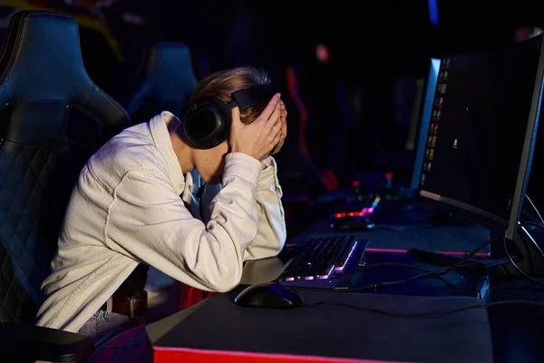 Upset gamer in headphones with hands on face after a losing cybersport match, disappointment — Stock Photo