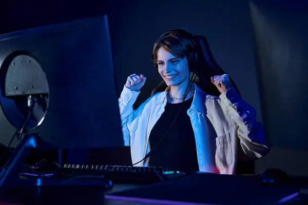 Happy short-haired woman looking at computer in a blue-lit room, cybersport and gaming concept — Stock Photo