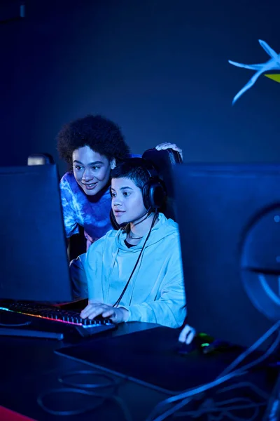 Jovem mulher em fones de ouvido com microfone jogando jogo de computador perto de amigo, cybersport — Fotografia de Stock