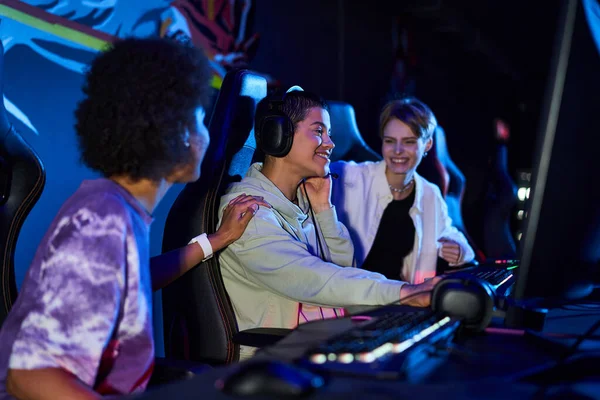 Feliz interracial mulheres zoomers envolvidos em jogos de cybersport, usando computadores e fones de ouvido — Fotografia de Stock