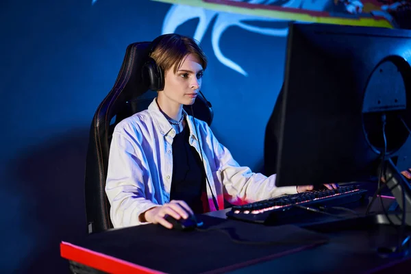 Gamer enfocado con pelo corto mirando a la computadora en una habitación con luz azul, jugador de ciberdeporte - foto de stock