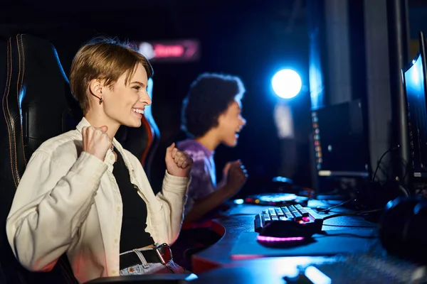 Foco na mulher alegre com cabelo curto olhando para monitor de computador perto do jogador feminino ao lado dela — Fotografia de Stock