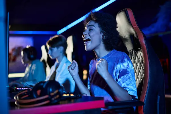 Excitée femme afro-américaine regardant l'écran d'ordinateur et acclamant dans la chambre éclairée bleue, gagnant — Photo de stock