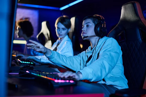 Foco na mulher focada com cabelo curto olhando para monitor de computador perto de jogadores do sexo feminino no quarto — Fotografia de Stock