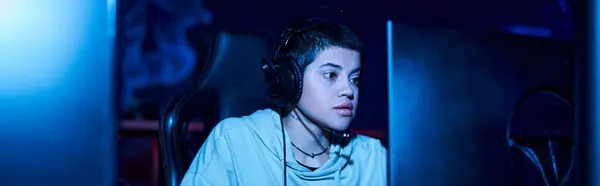 Focused gamer looking at computer monitor while playing game in a blue lit room, cybersport banner — Stock Photo