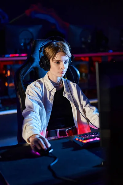 Female gamer in headphones looking at computer monitor while thinking on game strategy, cybersport — Stock Photo