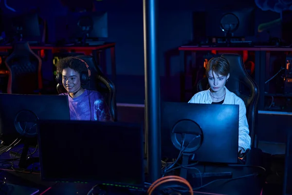 Diverse female friends in headphones looking at monitors while playing multiplayer computer game — Stock Photo